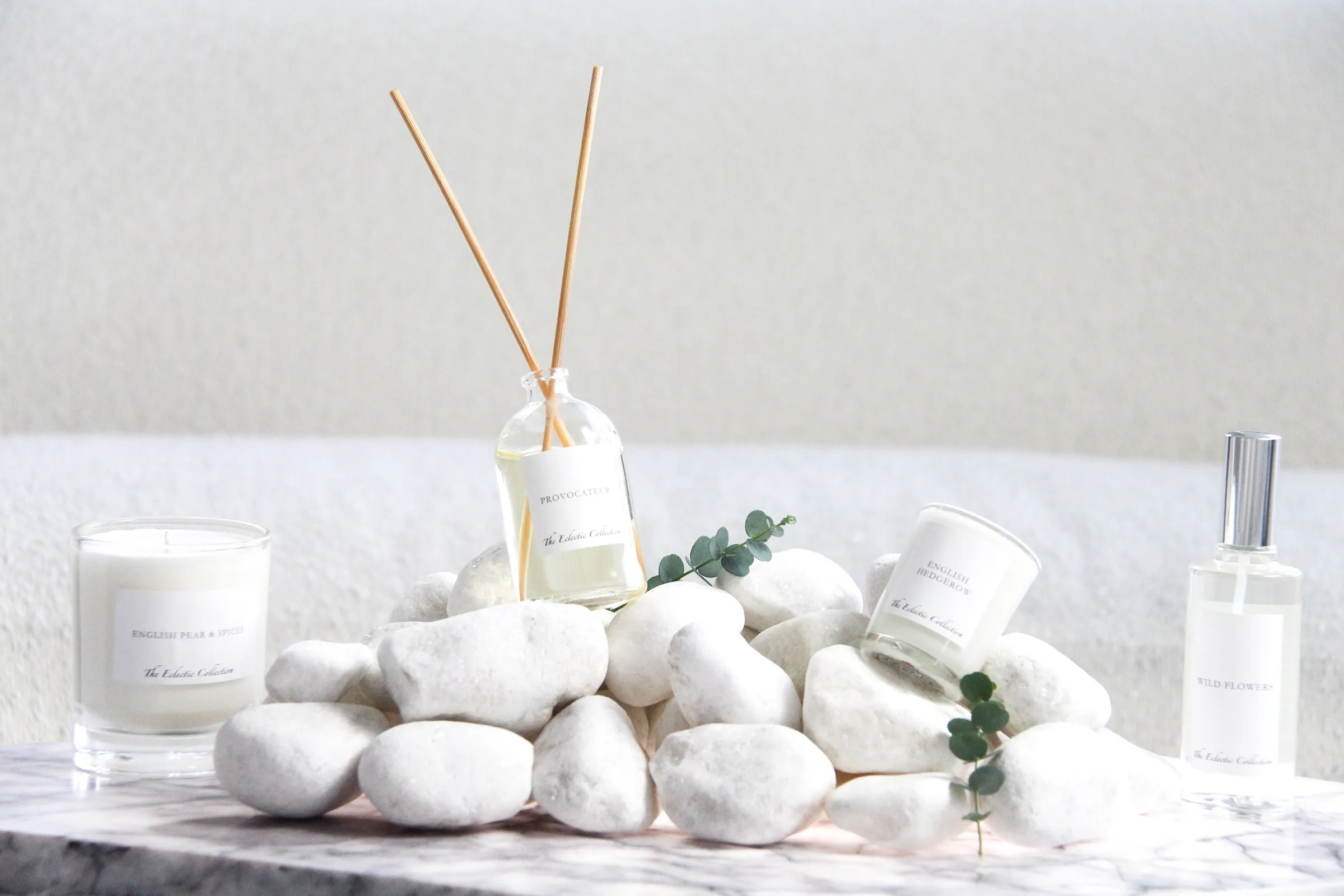 A reed diffuser and a candle on white stones